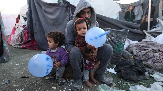 Hombre con sus dos niños pequeños, uno descalzo, en invierno en Deir al Balah en Gaza