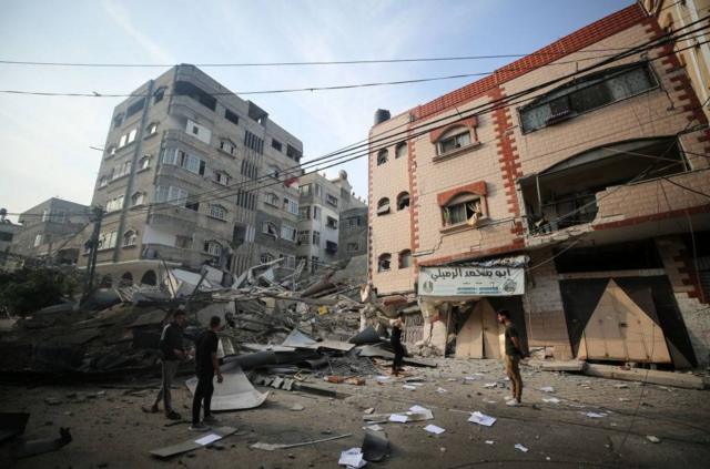 巴勒斯坦人站在伊斯兰国家银行大楼废墟旁
