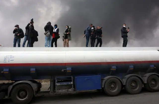 Novinari i fotoreporteri stoje na cisterni, gledajući kako se dim i dalje diže iznad pogođene rafinerije u Teheranu