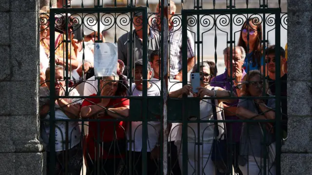 Ljudi gledaju sahranu kroz kapiju groblja 