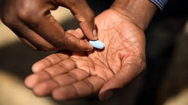 Pessoa recebendo comprimido azul na mão