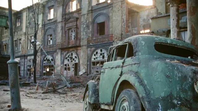 Un automóvil abandonado frente a una edificación derruida