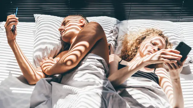 Couple lying in bed and using smartphones.