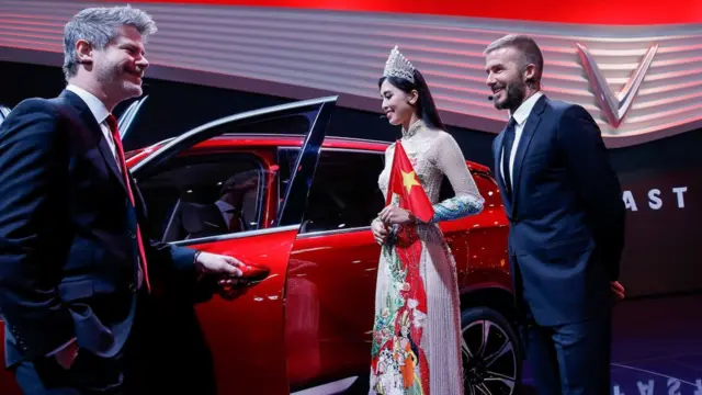 "Trên nền cờ đỏ sao vàng, theo sau hai chiếc ô tô là Hoa hậu Việt Nam 2018, trên tay cầm hai lá cờ. Chúng không có biểu tượng Vinfast, lại là cờ đỏ."
