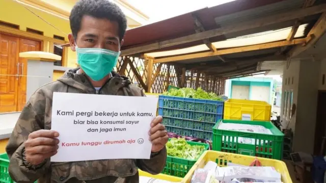 印尼農場主歐皮克（Pak Opik）舉著個標語，上面寫著"我們為您工作，這樣您就可以獲得蔬菜來保持身體健康"。