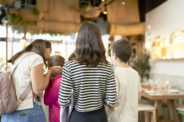Dos niños de espalda observan a su madre consolar a su hermanita