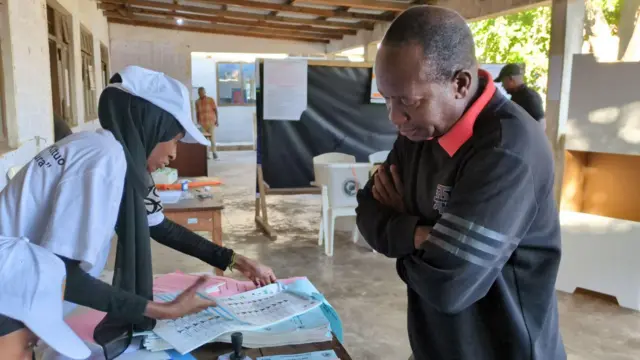 Nwata nwaanyị yi uwe ọcha bụ ọrụ ndị na-ahazi ntuliaka na-achọ aha nwoke yi uwe ojii ụkwụrụ n'ihu ya, n'ime akwụkwọ ndị debanyere aha ịtụ vootu.