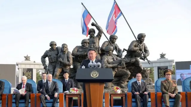 Кім Чен Ин на фоні меморіала