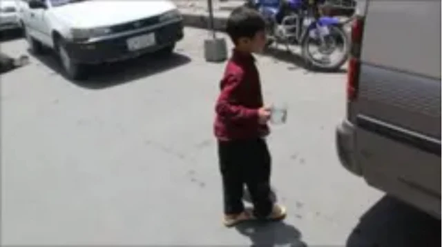 Ўғил бола кийимида ёш қизалоқ кўчада, машина ёнида турибди