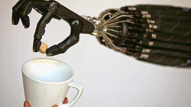
Uma mão robótica habilidosa colocando um cubo de açúcar em uma caneca.
