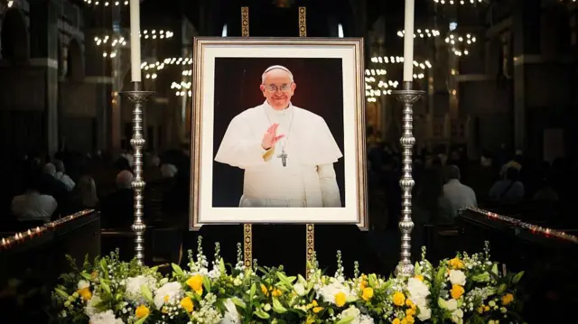 İngiltere'nin başkenti Londra'daki Westminster Katedrali'nde Papa Francesco'nun ölümü, fotoğrafının etrafına konulan sarı çiçeklerle anılıyor.