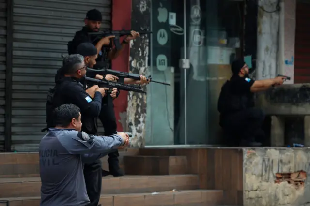 Policiais posicionados com armas perto de escadas e portas