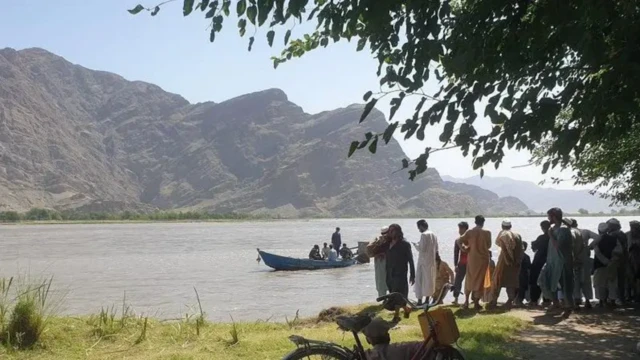 گروهی از مردان در کنار رودخانه در ننگرهار . چند نفر سوار قایق در وسط آب دیده میشوند