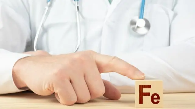 Un médecin posant un doigt sur un dé contenant le signe Fe (fer).