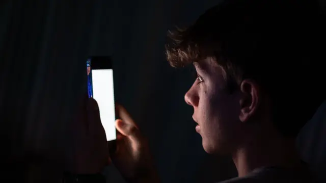 ينظر فتى مراهق يبلغ من العمر 13 عاماً إلى شاشة هاتف آيفون تعرض تطبيقات مختلفة من مواقع التواصل الاجتماعي في 23 ديسمبر/كانون الأول 2025 في مدينة باث بإنجلترا.