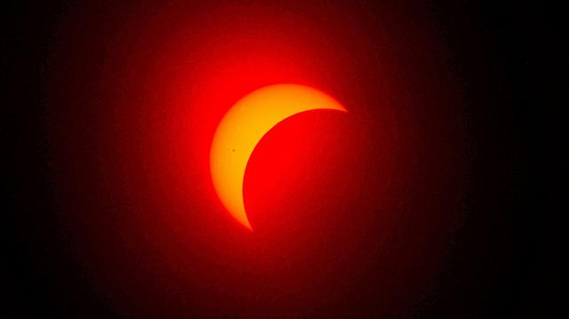 Foto colorida mostra processo do eclipse, com o Sol na parte de trás, laranja, e a lua o encobrindo como uma sombra