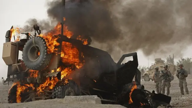 Американские солдаты смотрят на бронированное транспортное средство в огне