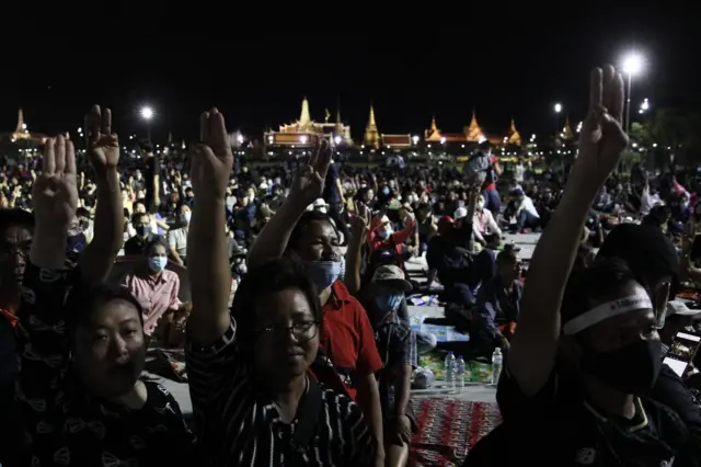 ผู้ชุมนุมชูสามนิ้ว ฉากหลังเป็นพระบรมมหาราชวัง