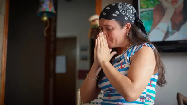 Bà Adriana Briceño đưa tay che mặt, cố kìm nước mắt, khi đang ngồi trong phòng khách nhà mình