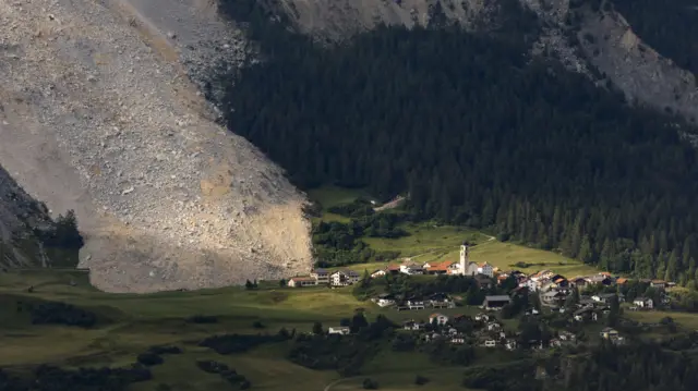 Foto aérea mostra enorme quantidade de pedras deslizadas, com vilarejo embaixo