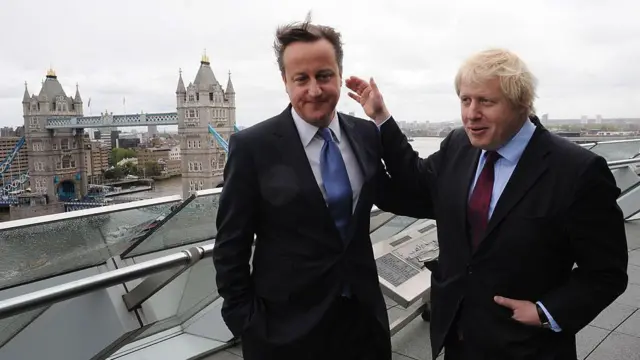 Дэвид Кэмерон и Борис Джонсон похлопывают друг друга на спине, стоя на смотровой площадке с видом на Темзу и Тауэрский мост