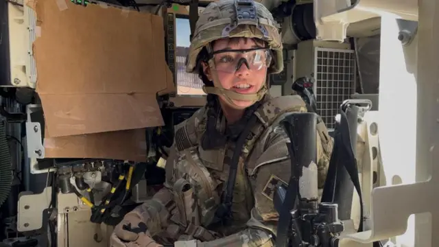 Mulher com roupas militares dentro de um carro de guerra
