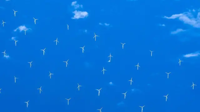 Grupo de turbinas eólicas no mar visto de cima, com o céu refletido na superfície