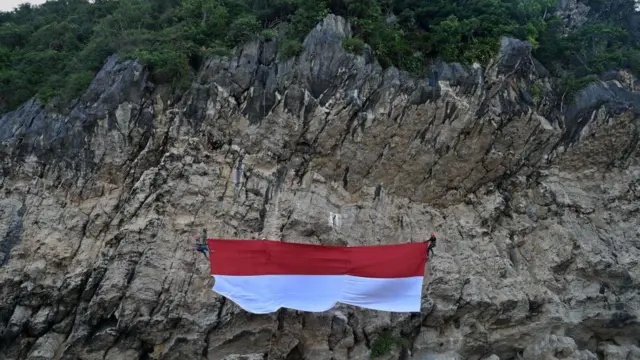 Sekelompok mahasiswa membentangkan bendera Indonesia menjelang HUT RI ke-77 di Pantai Lhoknga, Aceh.