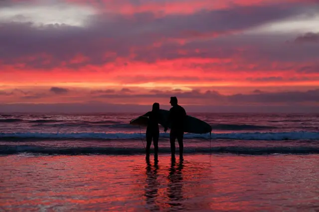 Dos surfistas miran un precioso atardecer rosado en las playas de LaJolla en California