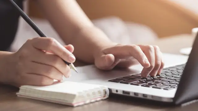 Manos sobre un teclado de computadora y una libreta