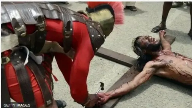 Ọkunrin kan to mura bii ologun n kan ọwọ Jesu, to sun silẹ, mọ igi agbelebu