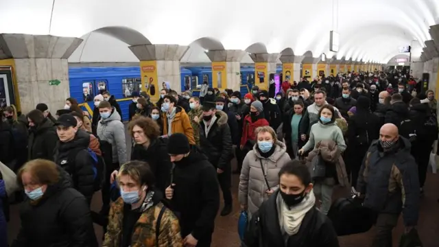 மக்கள், சிலர் பைகள் மற்றும் சூட்கேஸ்களை எடுத்துக்கொண்டு, கீஃப்-ல் உள்ள ஒரு மெட்ரோ நிலையத்திற்குச் செல்கின்றனர்