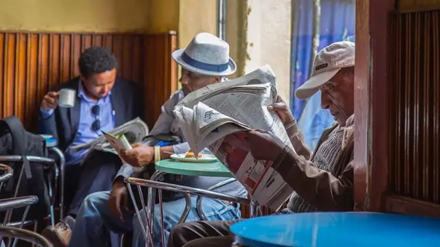 በካፍቴሪያ ውስጥ ጋዜጣ የሚያነቡ ሰዎች
