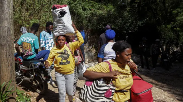 Las personas llevan consigo sus pertenencias mientras huyen de sus hogares tras una redada mortal llevada a cabo durante la noche por una banda armada, en las afueras de Puerto Príncipe.