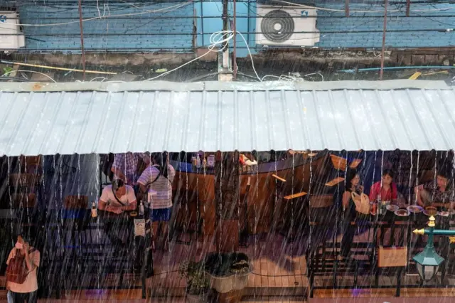 People sit inside a restaurant during a heavy rain downpour in Bangkok on September 13, 2022