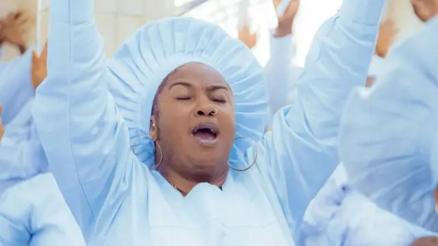 Oloogbe Tope Osoba wọ aṣọ adura ati fila funfun, o nawọn mejeeji soke