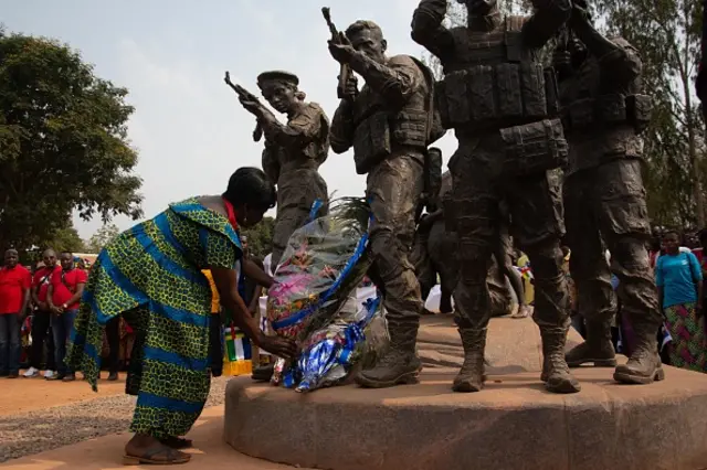 Une femme dépose une couronne de fleurs au pied d'un monument à Bangui le 23 février 2022 représentant des soldats centrafricains et des hommes armés russes protégeant une femme et ses enfants.