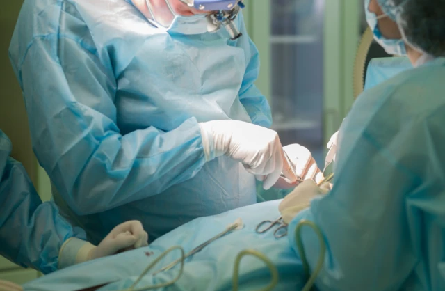 Médicos vestidos de azul, con mascarillas y con guantes blancos en un pabellón realizando una operación