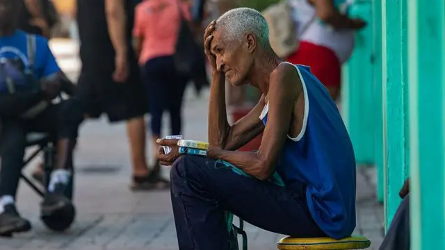 Hombre sentado en una calle en Cuba vende paquetes de cigarrillos. 