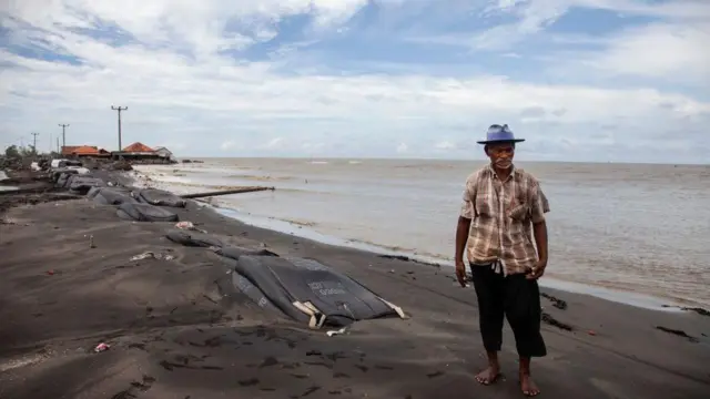 Carmat, 83 tahun, berfoto di dekat rumahnya yang hancur diterjang gelombang tinggi di Desa Cemarajaya, Kabupaten Karawang, Provinsi Jawa Barat, pada 26 Januari 2024.
