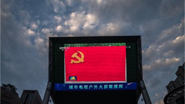 北京街头一台大型户外屏幕在直播的中国中央电视台《新闻联播》中展示着一面中国共产党党旗（1/7/2020）