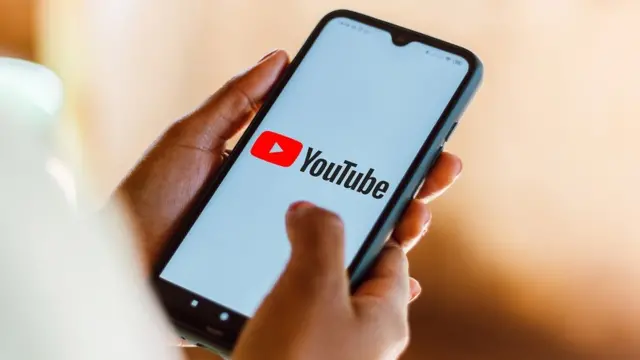 Mãoapp 9winzmulher segurando um smartphone, no qual o logotipo do YouTube é exibido na tela