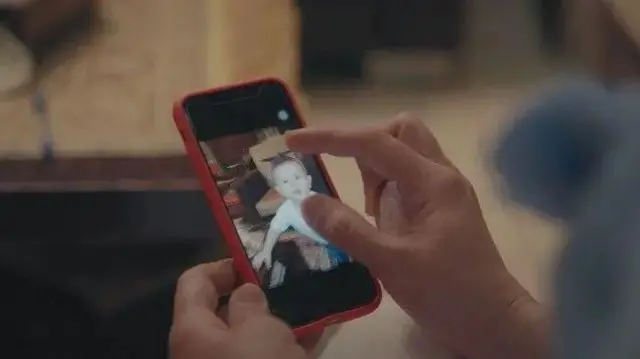  دستی که موبایلی را گرفته و تصویر کودکی در موبایل