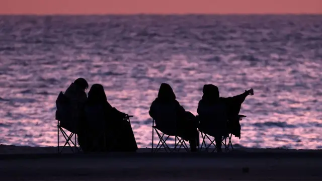 نساء يجلسن على الشاطئ عند شروق الشمس في مدينة الكويت في 15 أبريل 2023