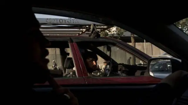 د موټر چلوونکي انځور چې د هغه تر څنګ د موټر دننه اخیستل شوی دی. هغه کیمرې ته ګوري.