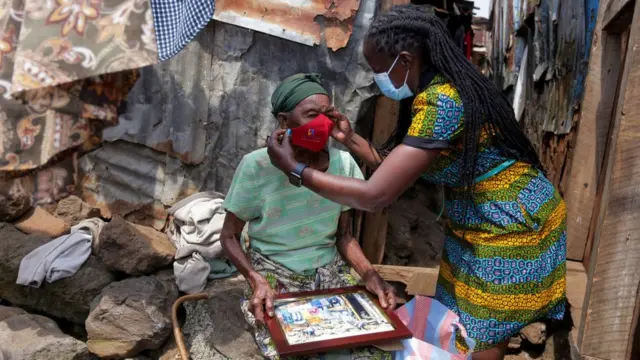 Une femme membre d'une organisation locale est vue en train de donner un masque à une dame âgée des bidonvilles de Mathare au milieu de la pandémie de coronavirus.
