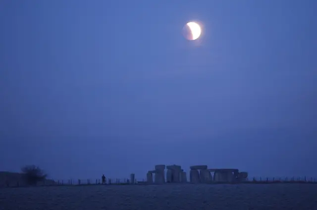 People view di full moon as one section move enta shadow during one lunar eclipse, before day break, for Stonehenge stone circle, near Amesbury, UK