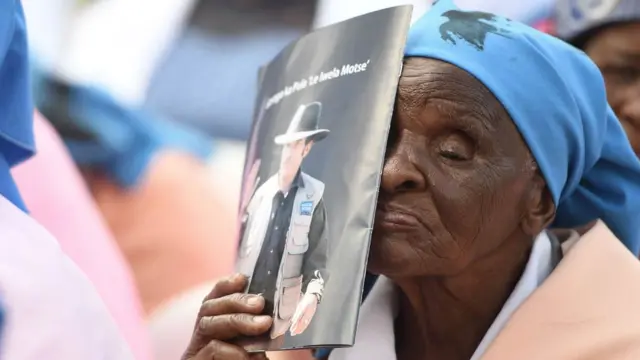 A woman holds a brochure carrying a portrait of Botswana's President as he arrives at a rally in his village on March 27, 2018