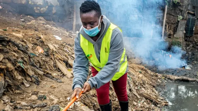 Sharon Sakase, étudiante et employée de salon de beauté avant la pandémie, dégageant un égout à ciel ouvert à Kibera, Kenya