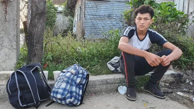 Michael sentado na beira da estrada com sacolas ao lado dele